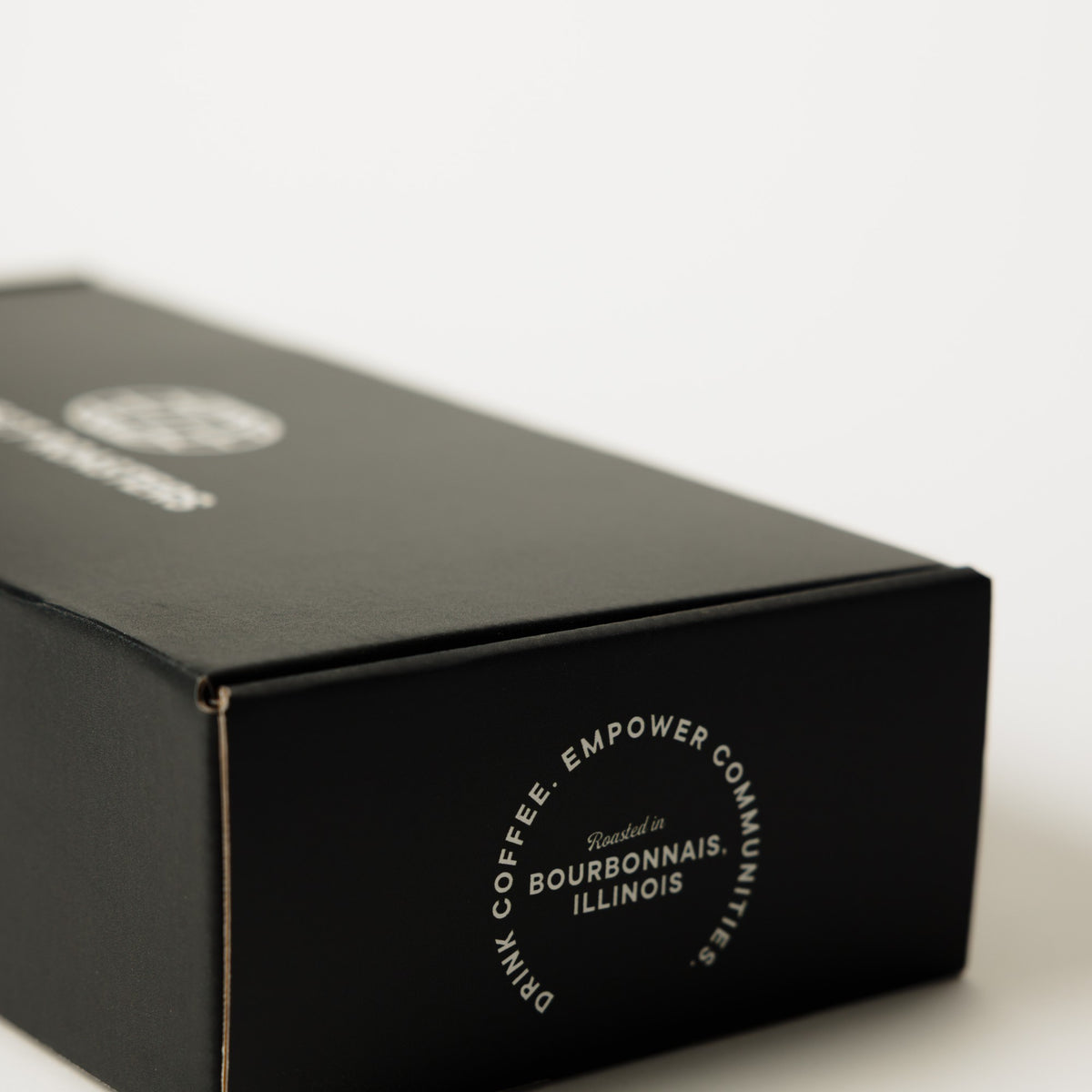 The printed Connect Roasters gift box closed, showing the Drink Coffee Empower Communities panel